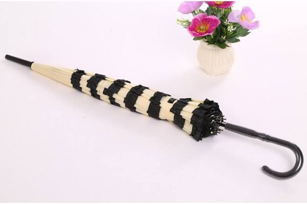 Black and white striped umbrella on a white background with a small vase of flowers.